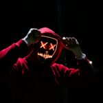 A spooky illuminated mask figure with a red hoodie in a dark setting, perfect for Halloween themes.